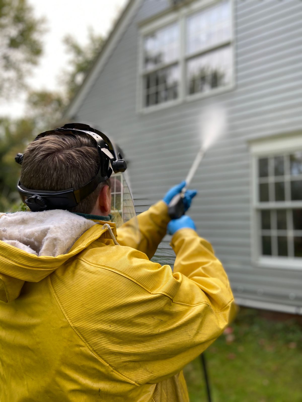Person pressure washing the siding of a house